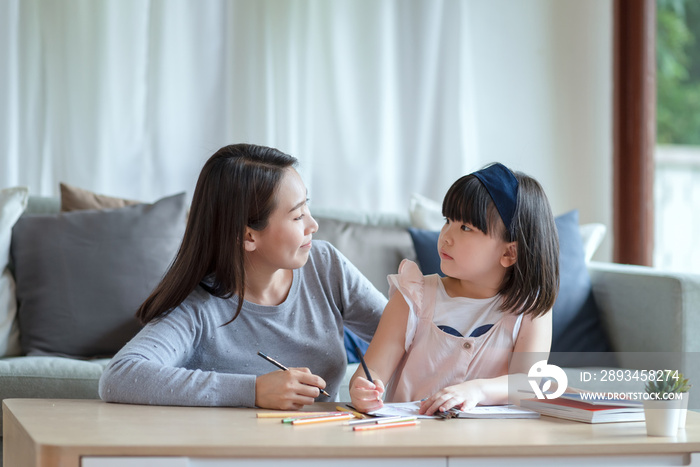 亚洲妈妈教她可爱的女儿在家里的客厅里学习