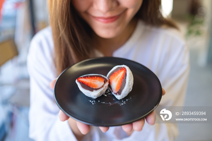 一位年轻女子拿着一盘草莓Mochi或甜红豆一护Daifuku的特写照片