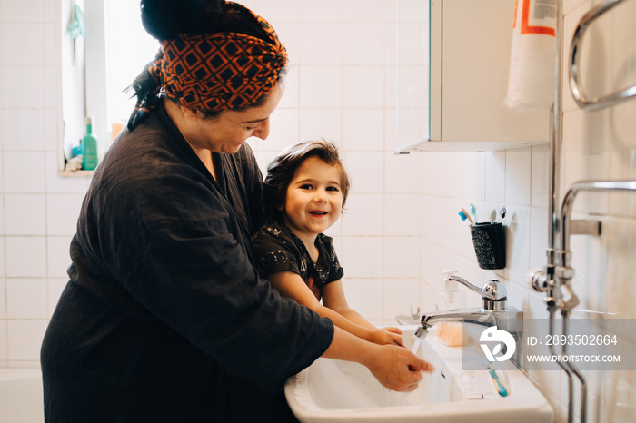 Smiling mother and son washing hands in sink at home