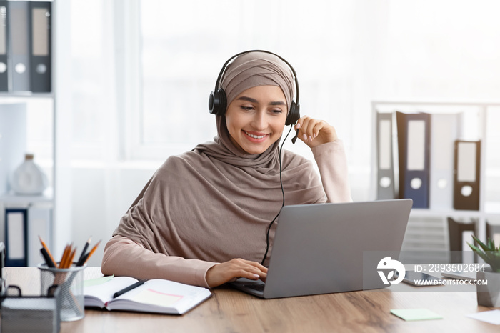 微笑的阿拉伯女孩坐在办公室里用笔记本电脑看网络研讨会
