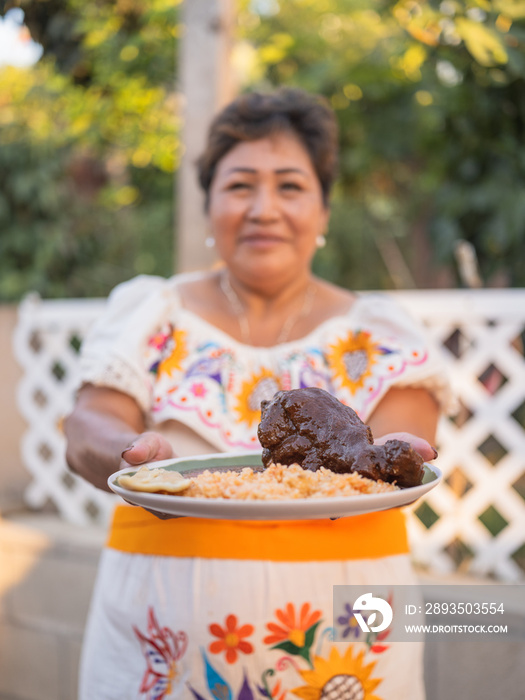 Indigenous woman wearing traditional clothing holding a plate of mole and rice