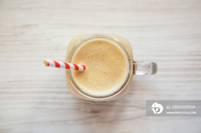 Peanut butter banana smoothie in a glass jar on a white wooden background, top view. Overhead, flat 