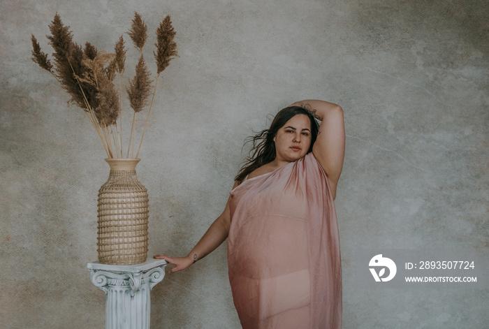 plus size metis woman wearing pink fabric hand on roman column arm overhead