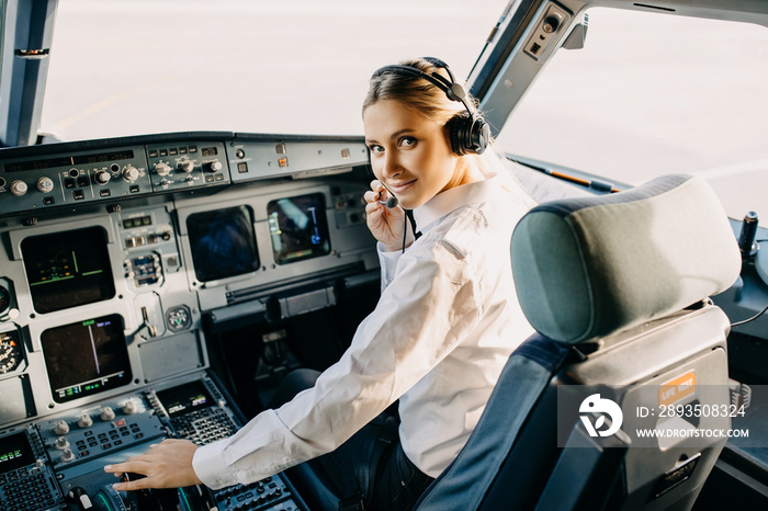 Confident woman pilot in airplane cockpit, wearing headset, looking at camera.