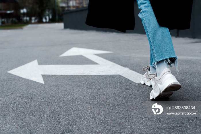 cropped view of woman in jeans walking near directional arrows on asphalt