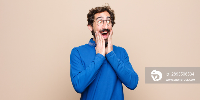 young handsome man feeling happy, excited and surprised, looking to the side with both hands on face