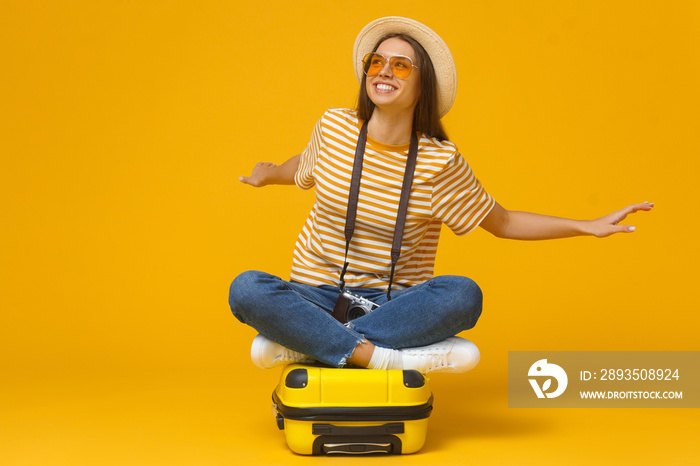 Dreams about traveling. Young dreamy female student tourist sitting on suitcase, pretending flying l