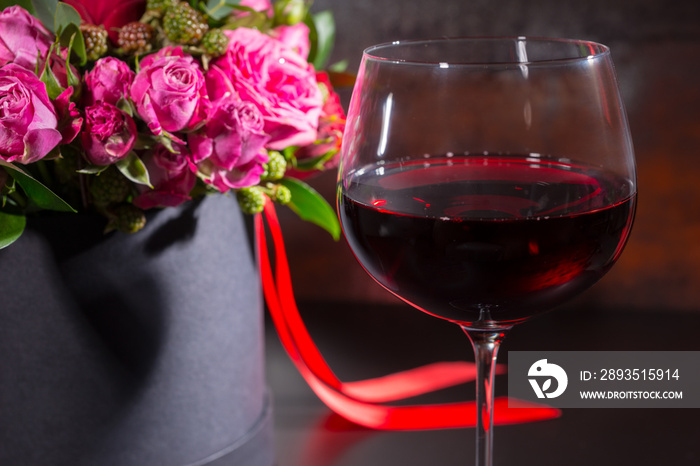 Beautiful bouquet of pink and red roses and red ribbon in a circular black box near a glass with win