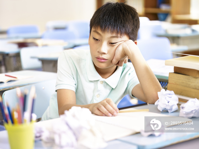 frustrated asian school boy sitting alone in classroom