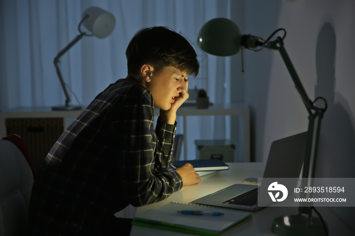 Upset teenage boy with laptop in dark room. Cyber bullying