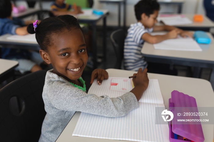 Schoolgirl looking at camera while studying in classroom