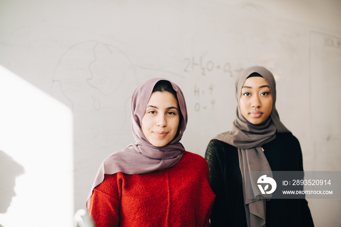 Portrait of teenage female friends wearing hijab standing at classroom