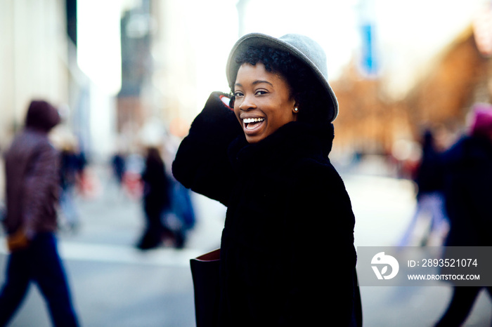 Portrait of a happy smiling woman in faux fur coat and hat laughing at camera while crossing a busy 