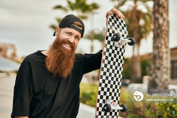 Young irish skater man smiling happy holding skate at the city.