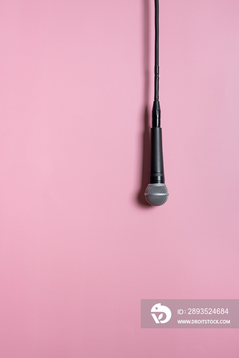 挂在粉色背景上的现代黑色有线麦克风，在录音室中投射阴影。