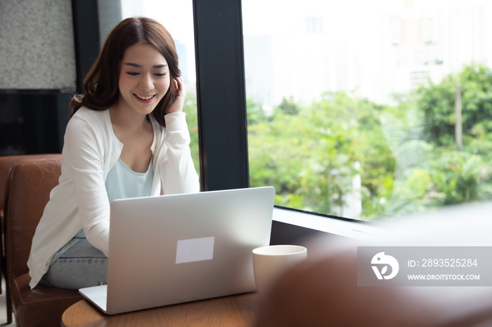 Beautiful smiling Asian female blogger dressed casual sitting and using laptop computer on the wood 