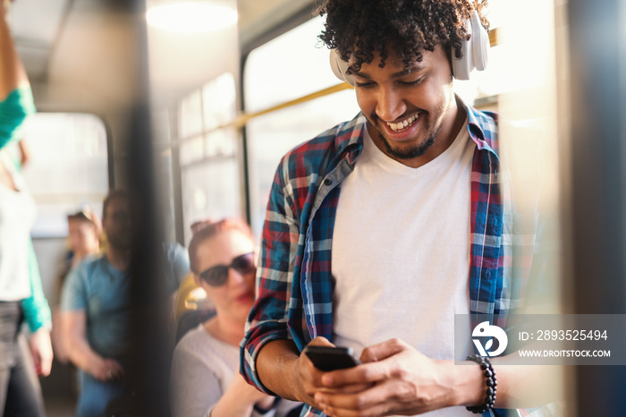 Young African guy listening to the music and using smart phone while riding in public transportation