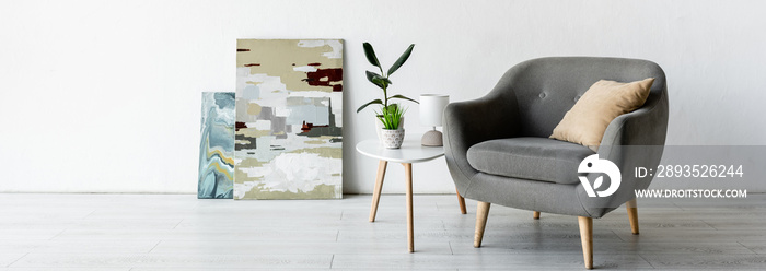 panoramic crop of comfortable armchair near coffee table with green plants, lamp and paintings in li