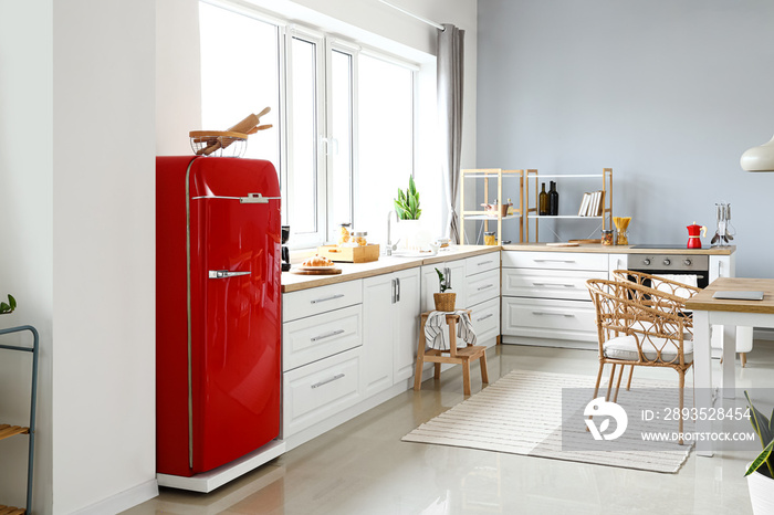 Interior of light modern kitchen with red fridge, white counters and dining table