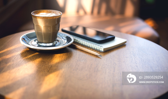 Latte coffee in old style glass and mobile phone, note book on wooden table with vintage sofa and su