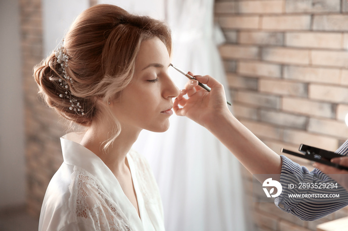 Makeup artist preparing bride before her wedding in room