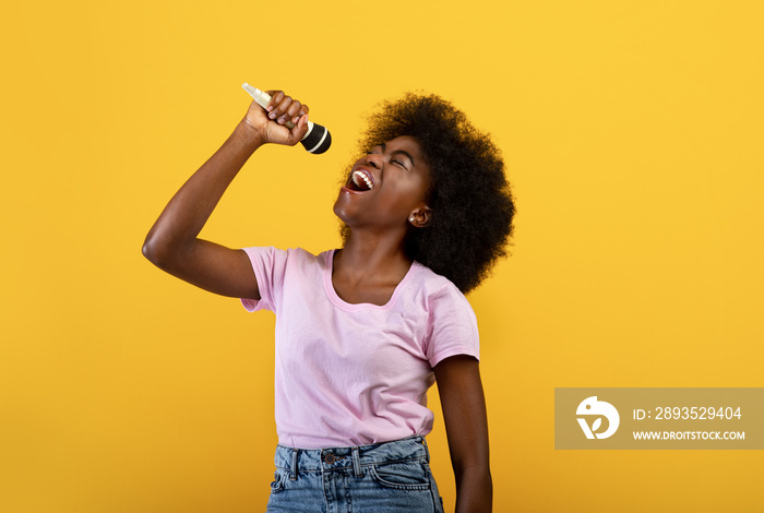 Joyful african american lady singing songs in microphone, having fun and enjoying the moment, yellow