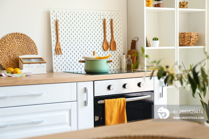 Cooking pot on stove and peg board with wooden spatulas in kitchen