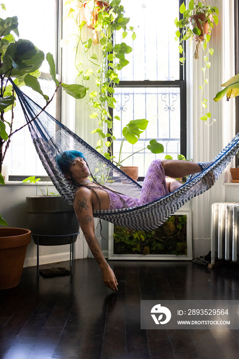 indigenous non-binary artist with blue hair relaxing in hammock