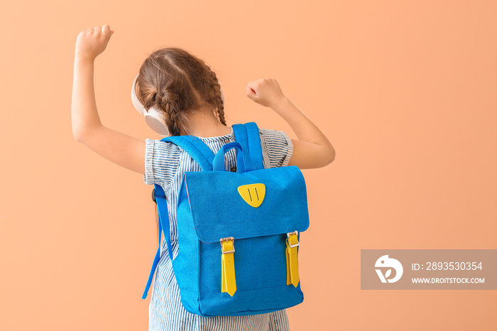 Cute little schoolgirl listening to music on color background