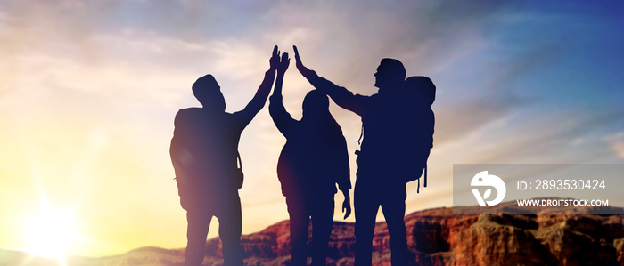 travel, tourism and hike concept - group of travellers with backpacks making high five over sunrise 