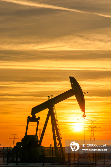 Pumpjack and transmission towers at sunset symbolizing energy transition. A pump jack pumping oil ou