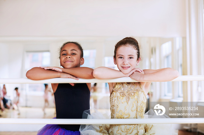 Portrait of smiling friends leaning on barre in studio