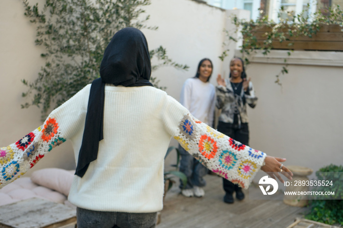 Three smiling women wearing hijabs greeting in garden