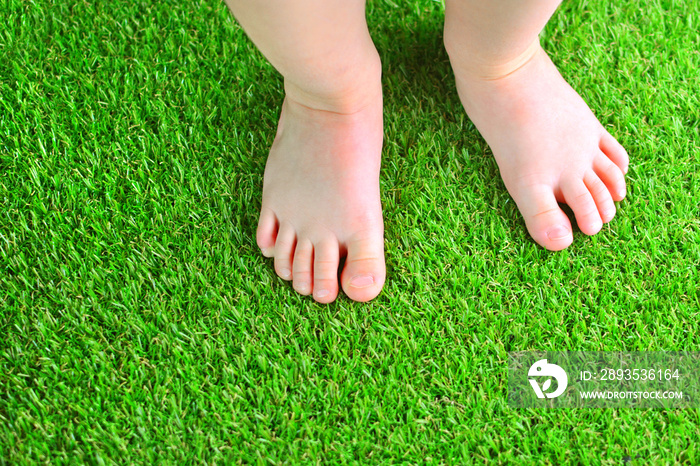 Artificial turf background. Tender foots of a baby on a green artificial grass floor.