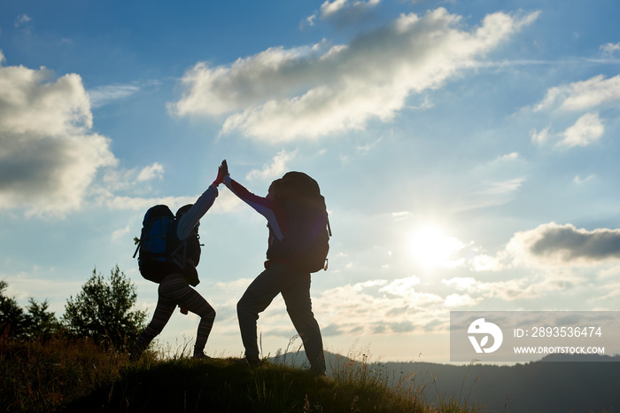 A cheerful couple with backpacks on top of the mountain give each other a high five against the back