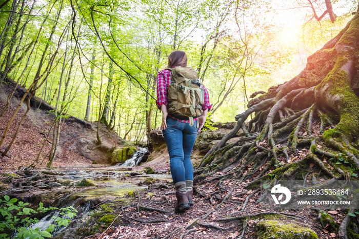 Frau mit rucksack in einem schönen wald beim wandern in der nähe eines wasserfalls