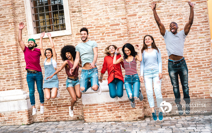 Multicultural milenial friends jumping and cheering against brick wall at city center - Friendship l