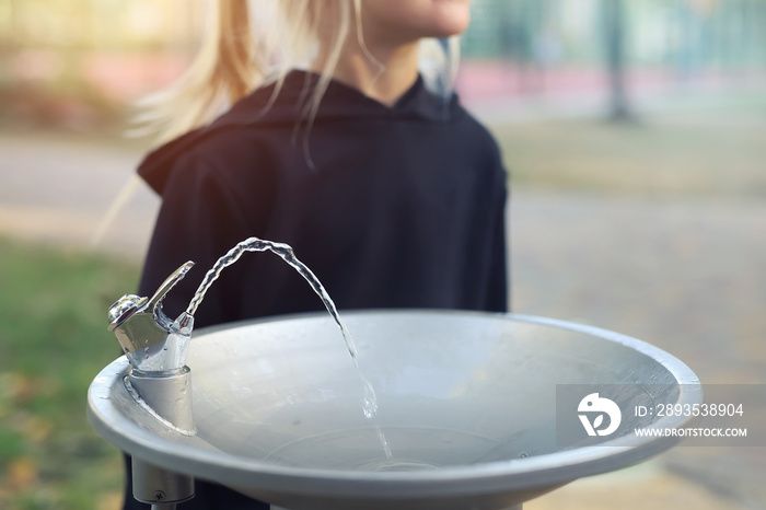 可爱的高加索金发小女孩口渴地从公共饮水机喝水