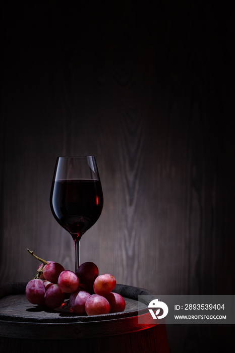 Glass of red wine and pink grapes on wooden barrel