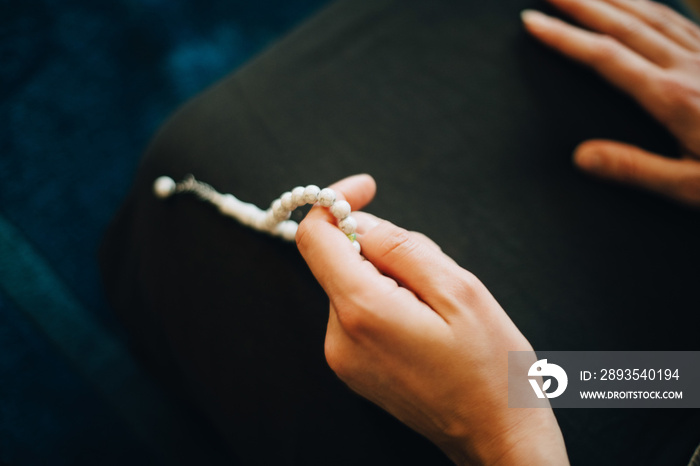 Cropped image of woman praying with rosary beads at home