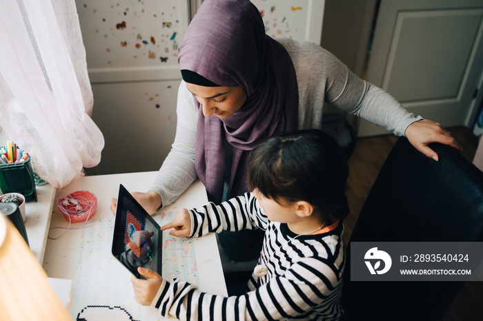 High angle view of mother assisting daughter in studying from digital tablet at home