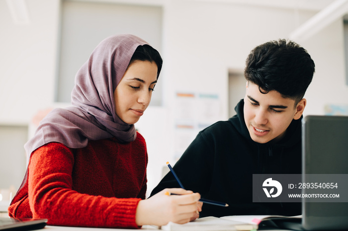 Teenage students learning together at desk in university