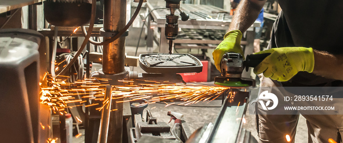 Man working with electric grinder tool on steel structure in factory, sparks flying. Grinding machin