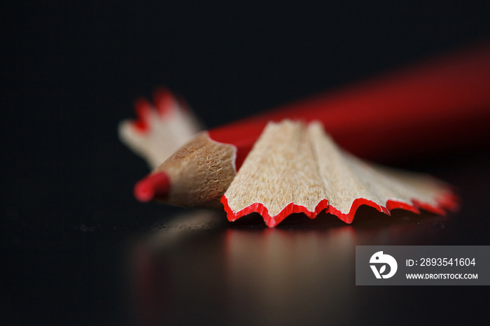 Red pencil and shavings on black background. Closeup