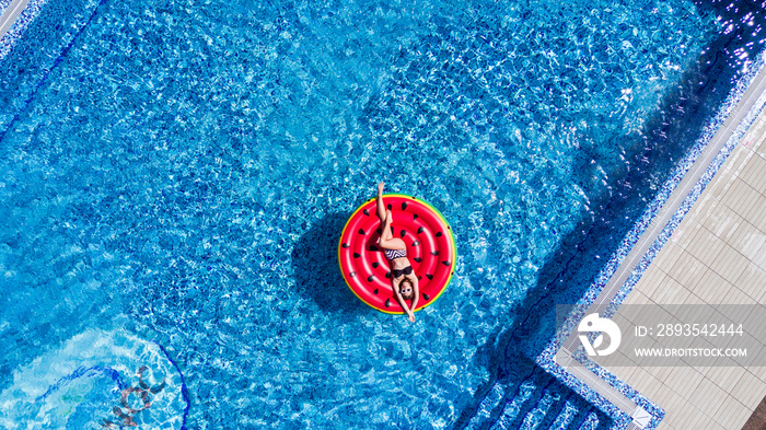 Top view of young woman relaxing on watermelon in pool. Young girl floating with fruit mattress. Sum