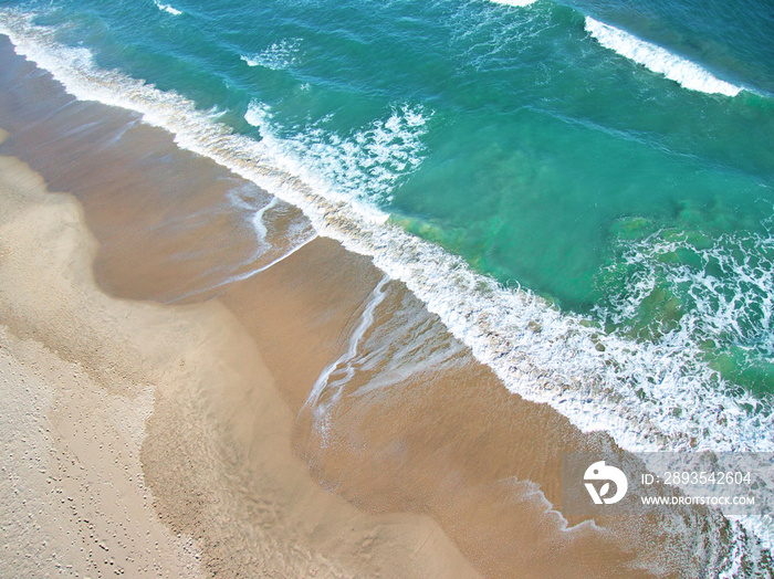 Aerial shot of the foam of the sea waves with orange sand and green water