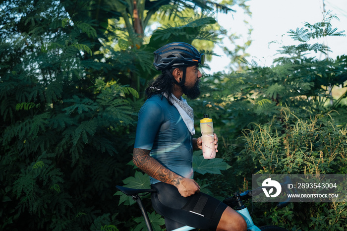 A young bearded cyclist drinking from a drinking bottle.