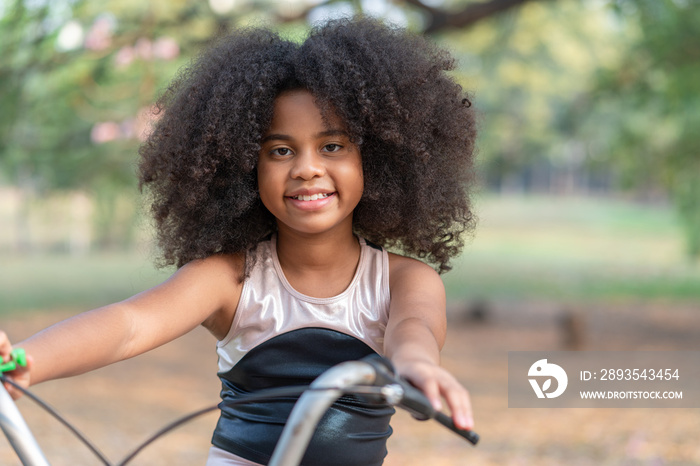 African American  girl smiling and looking at camera while riding a bicycle in the park