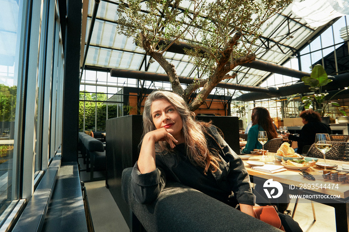 Thoughtful mature woman sitting on sofa in restaurant