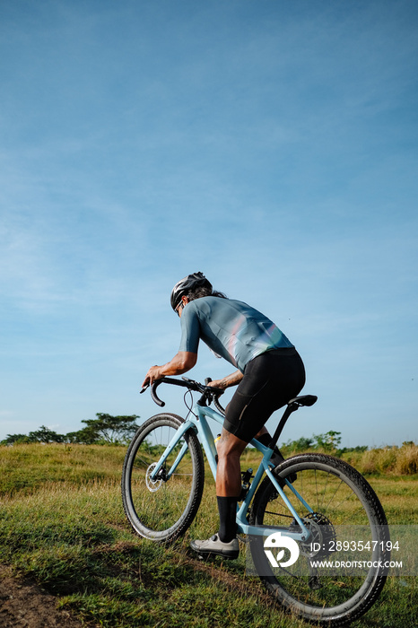 A young bearded cyclist is biking through a field